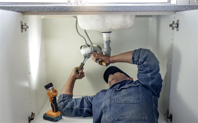 Plumber repairing pipes beneath a bathroom sink in Simi Valley